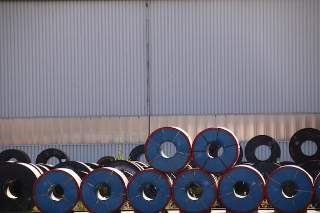 A close-up photograph of steel coils being loaded onto a truck at a US factory. Several workers in hard hats and safety vests are securing the load. The background shows various other large steel components within the factory setting.