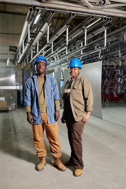 A group of workers in hard hats collaborating on a factory floor. The scene emphasizes teamwork and the human element in American manufacturing.